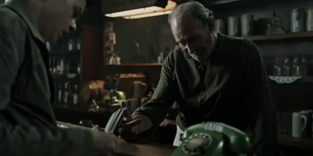 Ein Barkeeper neben einem alten grünen Wählscheibentelefon.